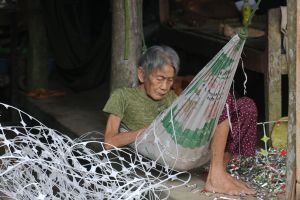 An old woman makes a few dong by scraping the residual tin foil from yoghurt pot lid cut-outs in a village on the Mekong